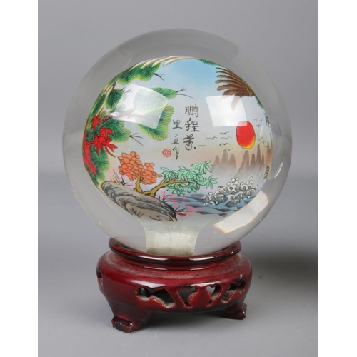 64 - A pair of oriental reverse hand painted spherical glass ornaments depicting eagles and cats, on carv... 