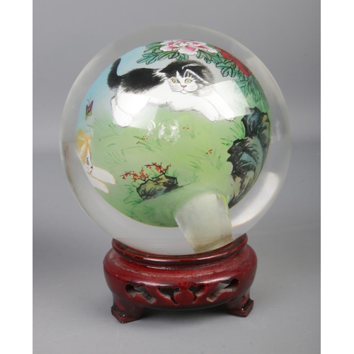 64 - A pair of oriental reverse hand painted spherical glass ornaments depicting eagles and cats, on carv... 