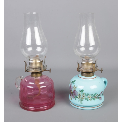 75 - Two small oil lamps to include cranberry glass and blue glaze, hand painted ceramic example.