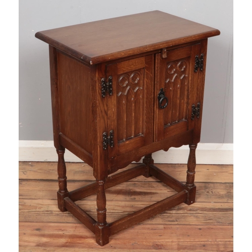 412 - A carved oak Old Charm style side cabinet raised on turned support. (68cm x 51cm)