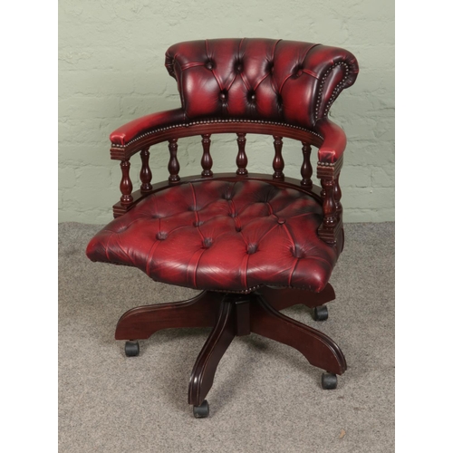 518 - A vintage captains chair featuring ox blood leather button upholstered seat and castors to feet.