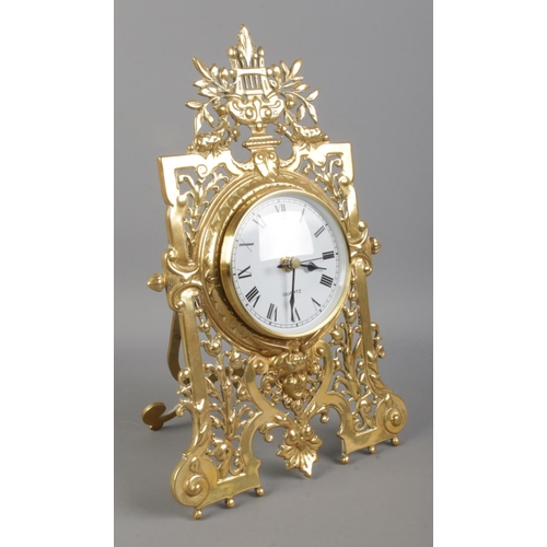 66 - A brass easel desk clock, with pierced scrolled and floral front. Height: 31cm. Fitted with later qu... 