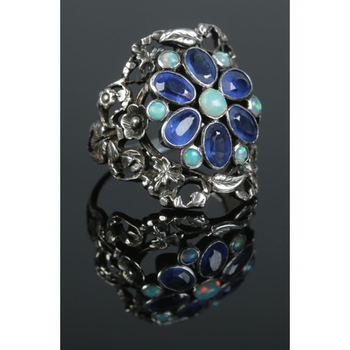 101 - An Arts & Crafts silver ring of floral design, set with sapphire coloured and opal stones. Size P. 6... 