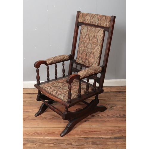 501 - A mahogany American style rocking chair with upholstered seat and backrest and turned arm supports.