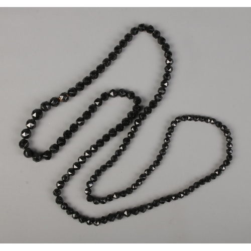 403 - A long graduated, faceted Jet beaded necklace.