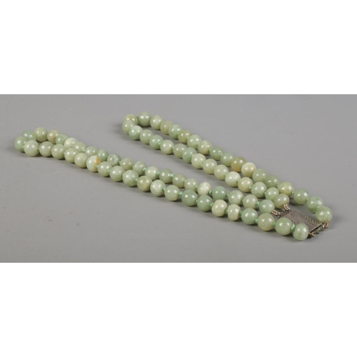 414 - A two row string of jade beads, set with Sterling silver clasp.