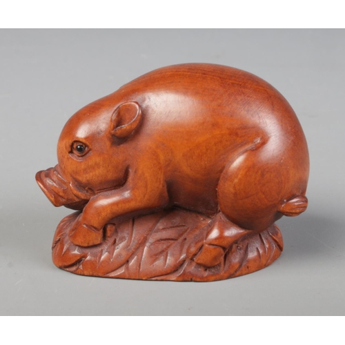 445 - A hand carved hardwood netsuke of a pig / boar laying on a bed of leaves, signed to base.