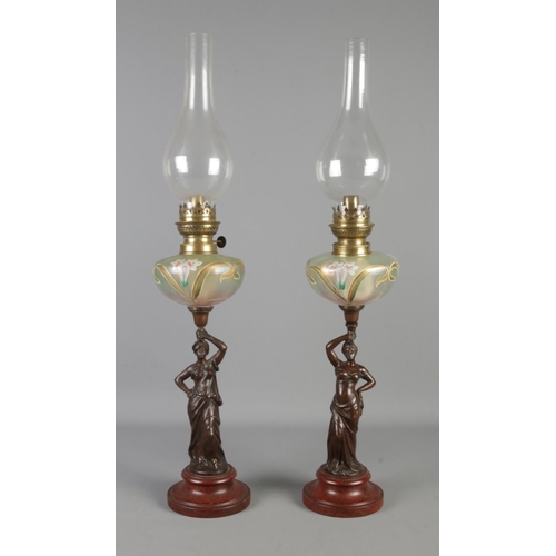 11 - A pair of Art Nouveau style oil lamps, with painted glass reservoirs and figures raised on turned ba... 