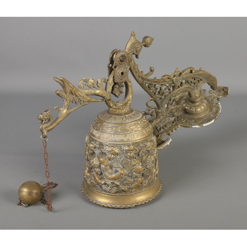 16 - An ornate brass wall hanging bell with chain decorated with floral motifs and cherubs.