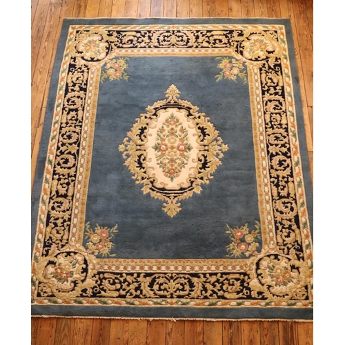 238 - A large blue ground machine knotted wool rug, with cream and dark blue border and central floral med... 