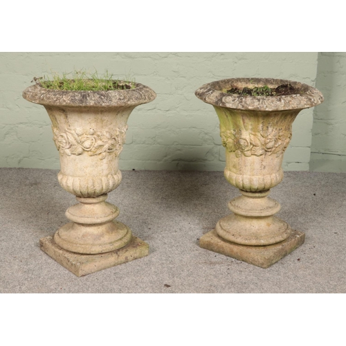 265 - A near pair of ornate concrete garden urns with ivy leaf band decoration, raised on square bases. He... 