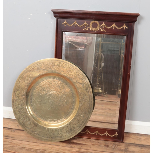 297 - A mahogany framed wall mirror with gilt decoration along with a large Eastern brass charger.