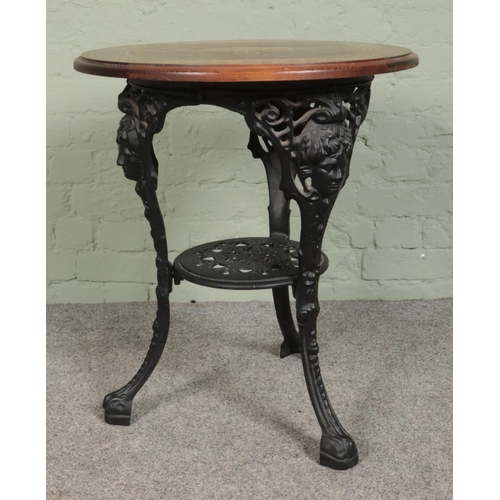 394 - A cast iron tavern table with decorative patterned oak top. Height: 70cm, Diameter of top: 60cm.