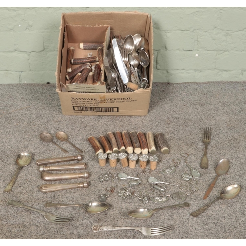 185 - A box of cutlery, metal mounted corks and keyrings. Includes horn handles, pair of silver spoons, et... 