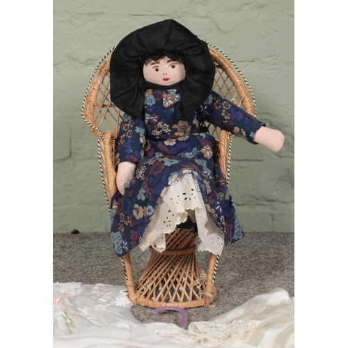 238 - A Papier Mache doll sat in a small cane chair, together with a collection of dolls clothes.