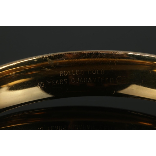 379 - A hinged rolled gold bangle, with '10 Years Guaranteed' inscribed to inside of band.