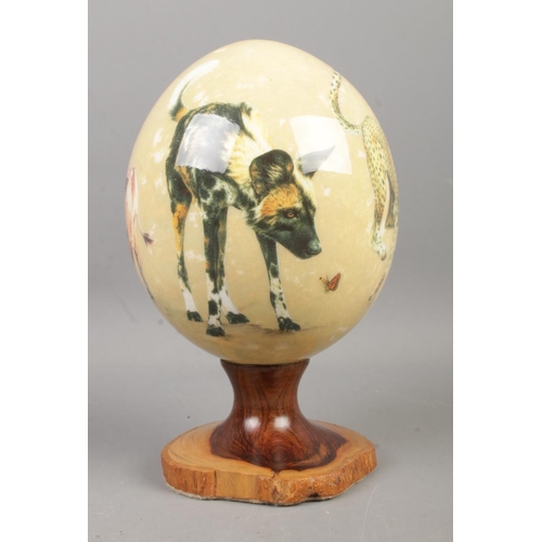 115 - Sherry Lowe painted ostrich egg on turned wood stand depicting various African animals including Che... 