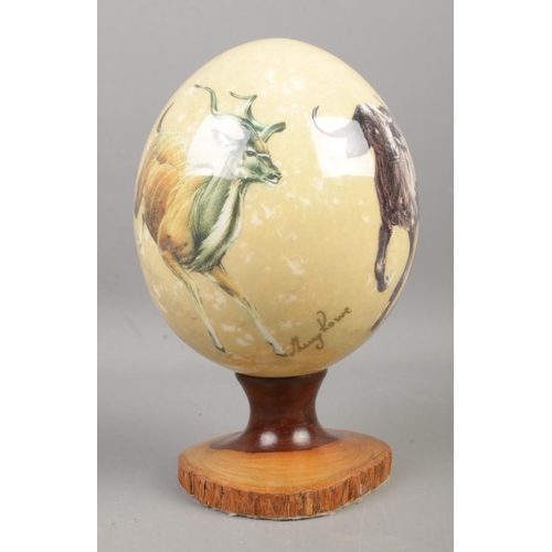 115 - Sherry Lowe painted ostrich egg on turned wood stand depicting various African animals including Che... 