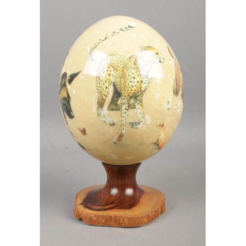 115 - Sherry Lowe painted ostrich egg on turned wood stand depicting various African animals including Che... 