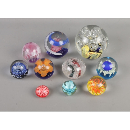 74 - Ten glass paperweights of varying sizes to include floral examples with bubble inclusions.