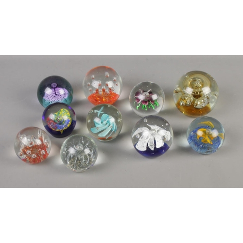 85 - A collection of ten glass paperweights to include floral and bubble examples.