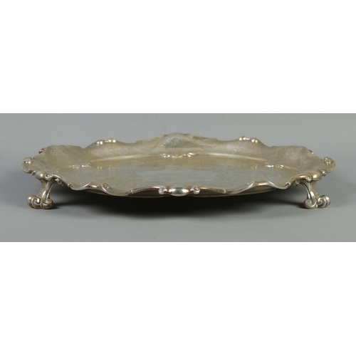 66 - A Victorian silver salver with scalloped edge and engraved decoration. Raised on three scrolled supp... 