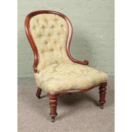 592 - A spoon back nursing chair with green floral buttoned upholstery set on four castors.