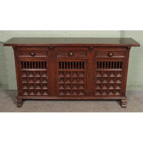 605 - A large hardwood sideboard, with drawer top and lower cupboard doors. Features spindle and paneled d... 