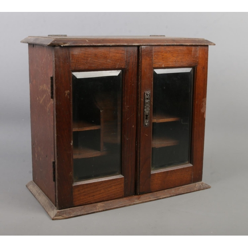 121 - A vintage oak table top smokers cabinet with bevel edge glass doors.