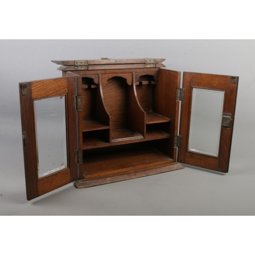 121 - A vintage oak table top smokers cabinet with bevel edge glass doors.