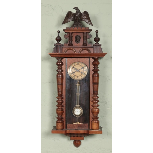 442 - A mahogany wall clock, with turned supports, eagle pediment and Roman Numeral dial. Chiming on a coi... 