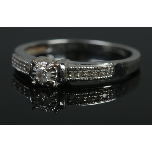 476 - A 9ct white gold ring featuring central solitaire flanked with diamond set shoulders. Size O, 2.38g.