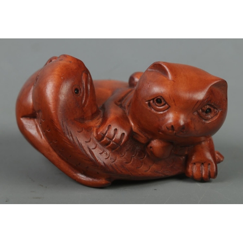 522 - A hand carved hardwood netsuke of a cat with fish, signed to base.