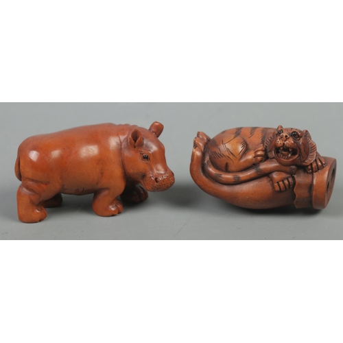 538 - Two carved hardwood netsukes, in the forms of a hippopotamus and a tiger in the palm of a hand. Both... 