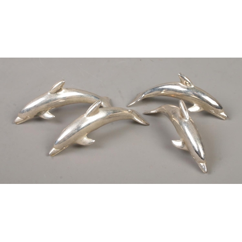 571 - A set of four white metal dolphin table place holders.