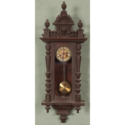 472 - A carved mahogany 8 day wall clock with mask decoration. Approximately 107cm.