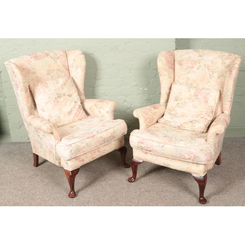 606 - A pair of upholstered wingback armchairs with floral decoration.