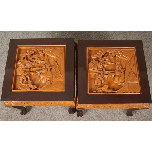 564 - A pair of Oriental hardwood occasional tables. Having deep carved decoration to tops depicting figur... 