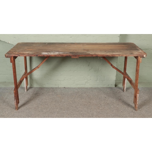 589 - A large wooden tressle table with folding legs. (86cm x 183cm x 66cm)