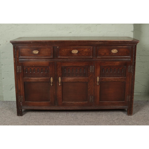 604 - An oak sideboard base, with brass handles and linen fold detailing. Height: 87cm. Width: 136cm, Dept... 