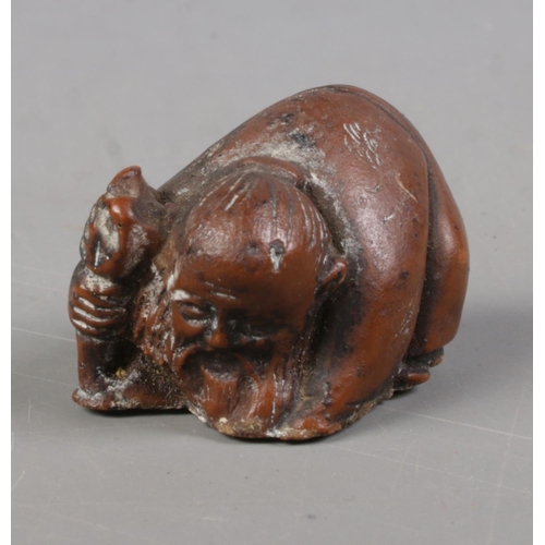 402 - A Japanese carved hardwood netsuke formed as crouching elder holding a staff.