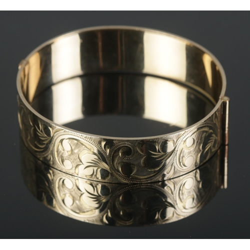 470 - A 9ct rolled gold bangle featuring engraved scroll decoration to one half.