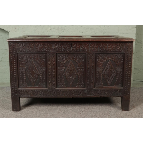 535 - An 18th century oak joined coffer with hinged top and profusely carved tri panel base fitted with in... 