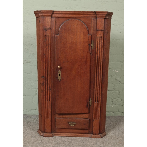 548 - An early Victorian oak hanging corner cupboard with  cupboard door over singular drawer flanked by f... 