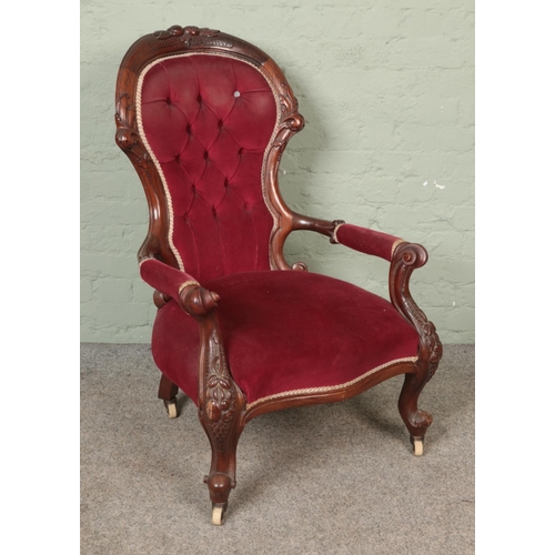 598 - A Victorian open arm chair with carved mahogany frame and red upholstery on castors.