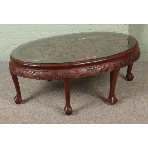 614 - A carved glass topped oriental style coffee table featuring carved legs with lion paw feet. Approx. ... 