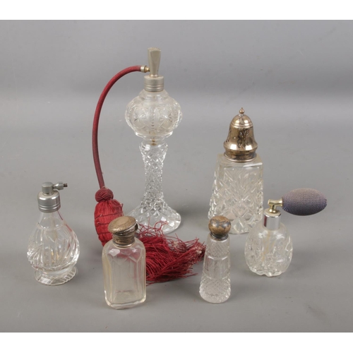 92 - A collection of cut glass atomisers and scent bottles including a silver topped sugar caster.