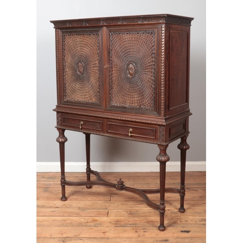 321 - A Liberty & Co carved mahogany cabinet. Having bergere door panels, interior drawers and raised on t... 