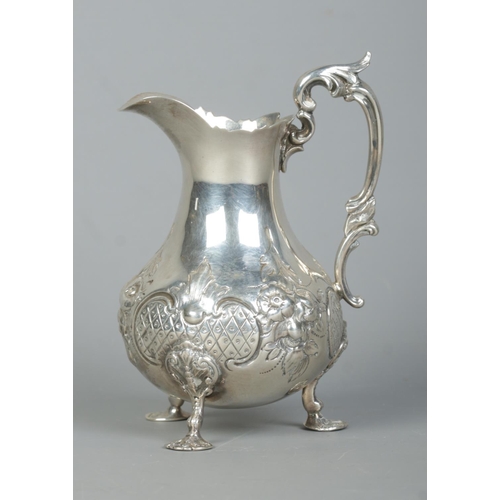 92 - A Victorian silver cream jug with repousse decoration, scrolling handle and raised on three hoof fee... 