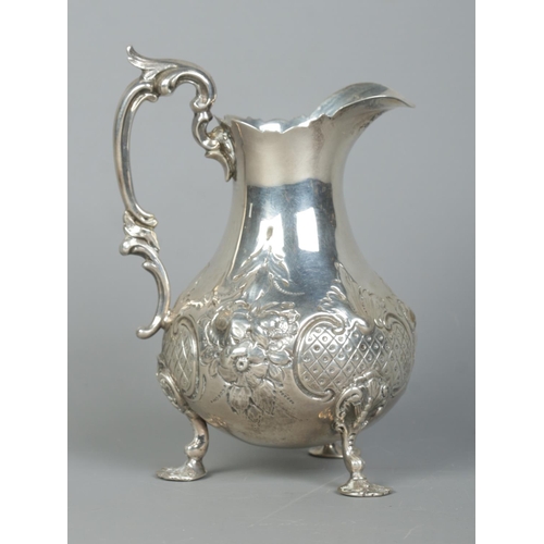 92 - A Victorian silver cream jug with repousse decoration, scrolling handle and raised on three hoof fee... 